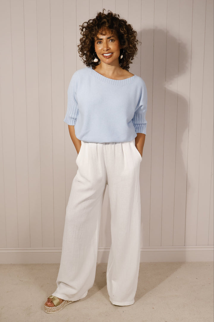Person wearing a light blue sweater and white pants on a neutral background