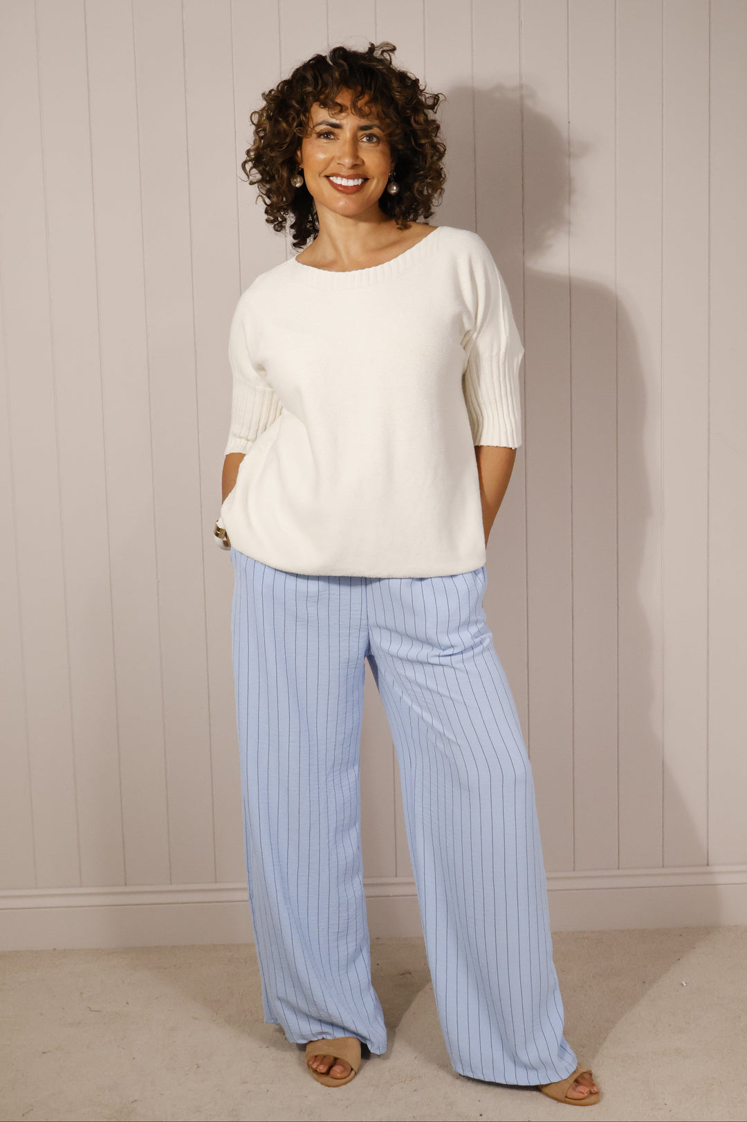 Woman wearing a white top and light blue pants on a plain background